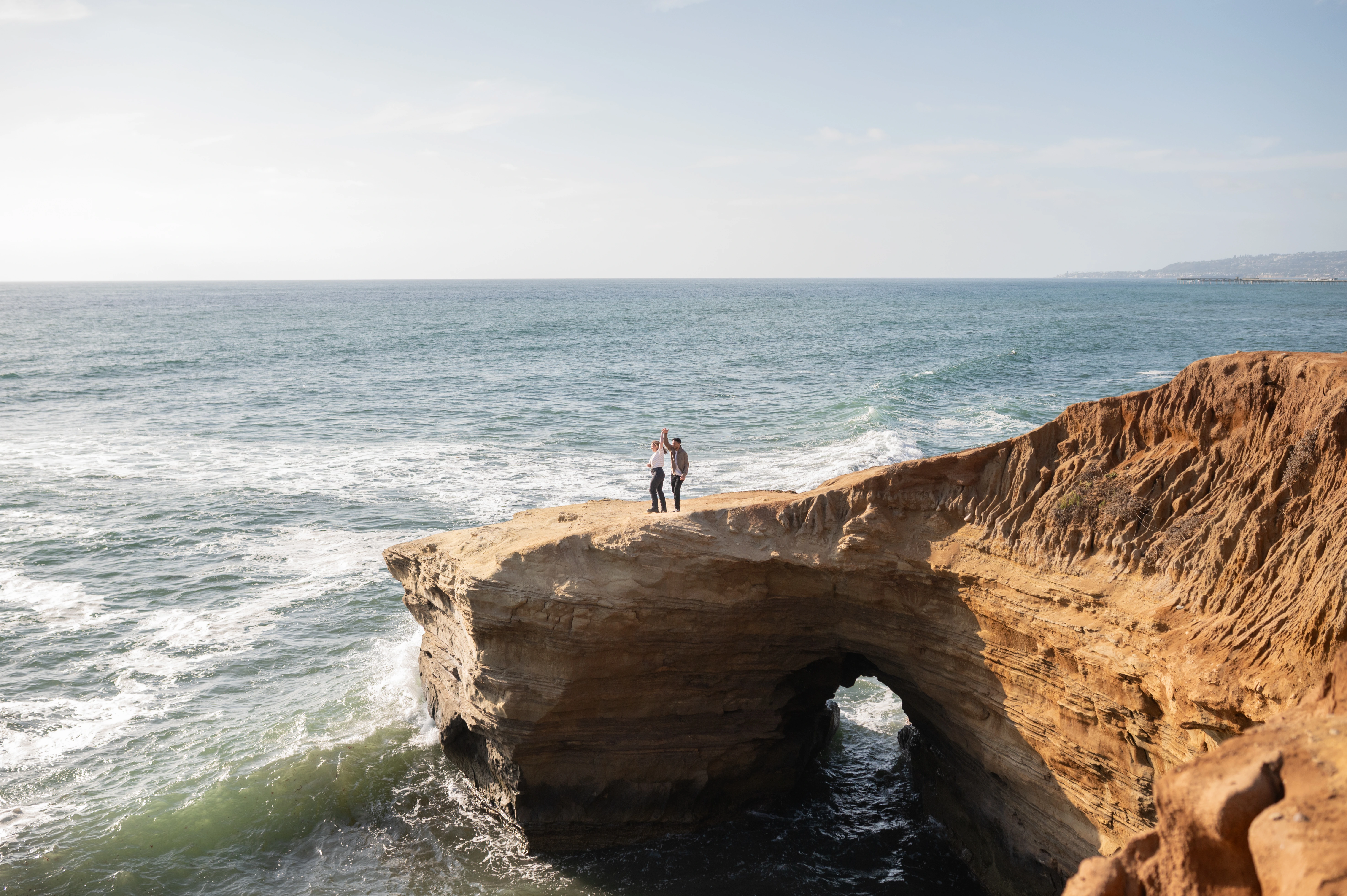 A couple stands on a stunning rock formation at Sunset Cliffs, overlooking the vast ocean. The golden hues of the sunset create a romantic backdrop, capturing the essence of love and commitment.