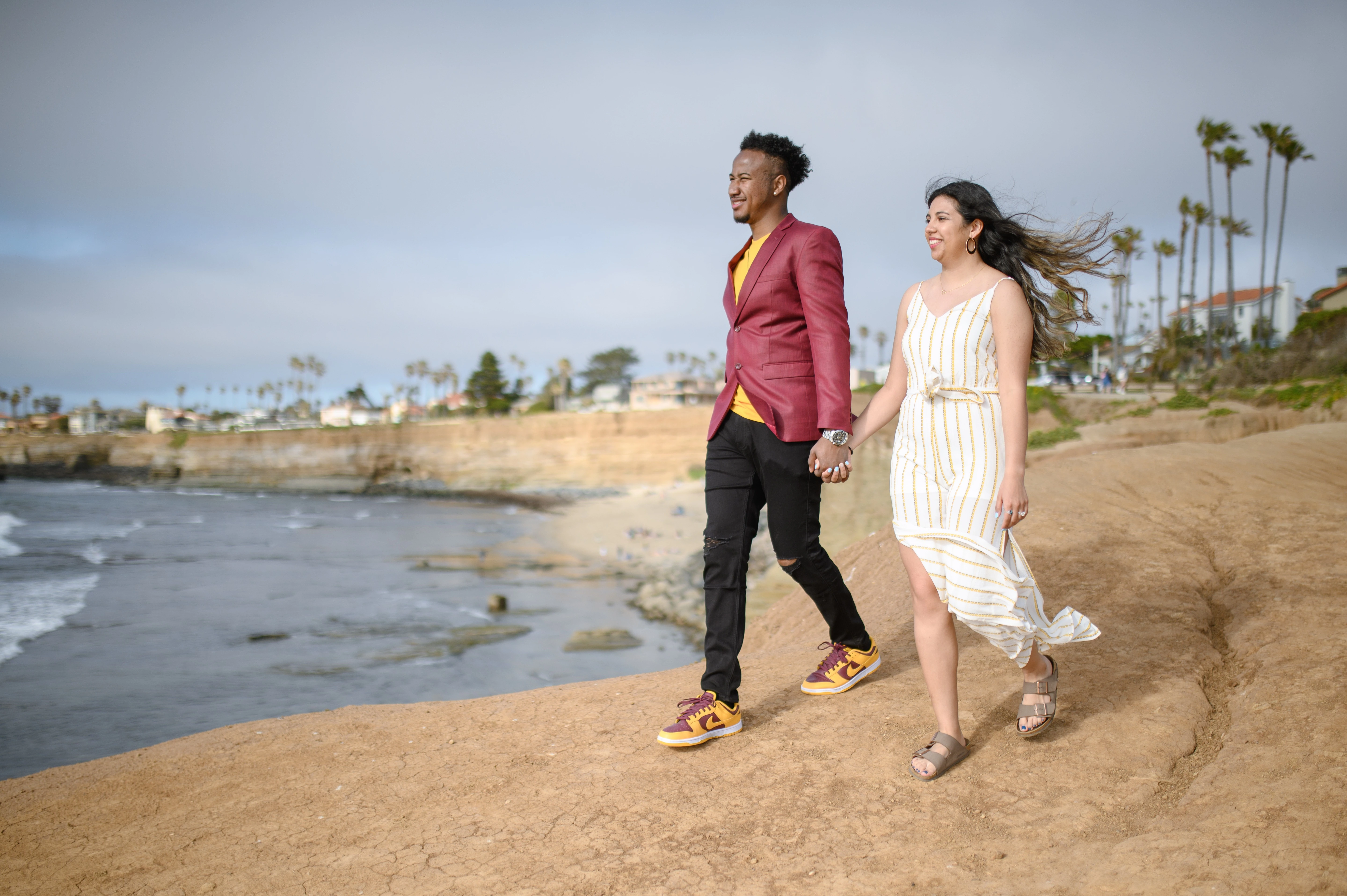A San Diego engagement photographer captures a couple walking along the shore at Sunset Cliffs, embodying romance and the excitement of planning a surprise proposal.
