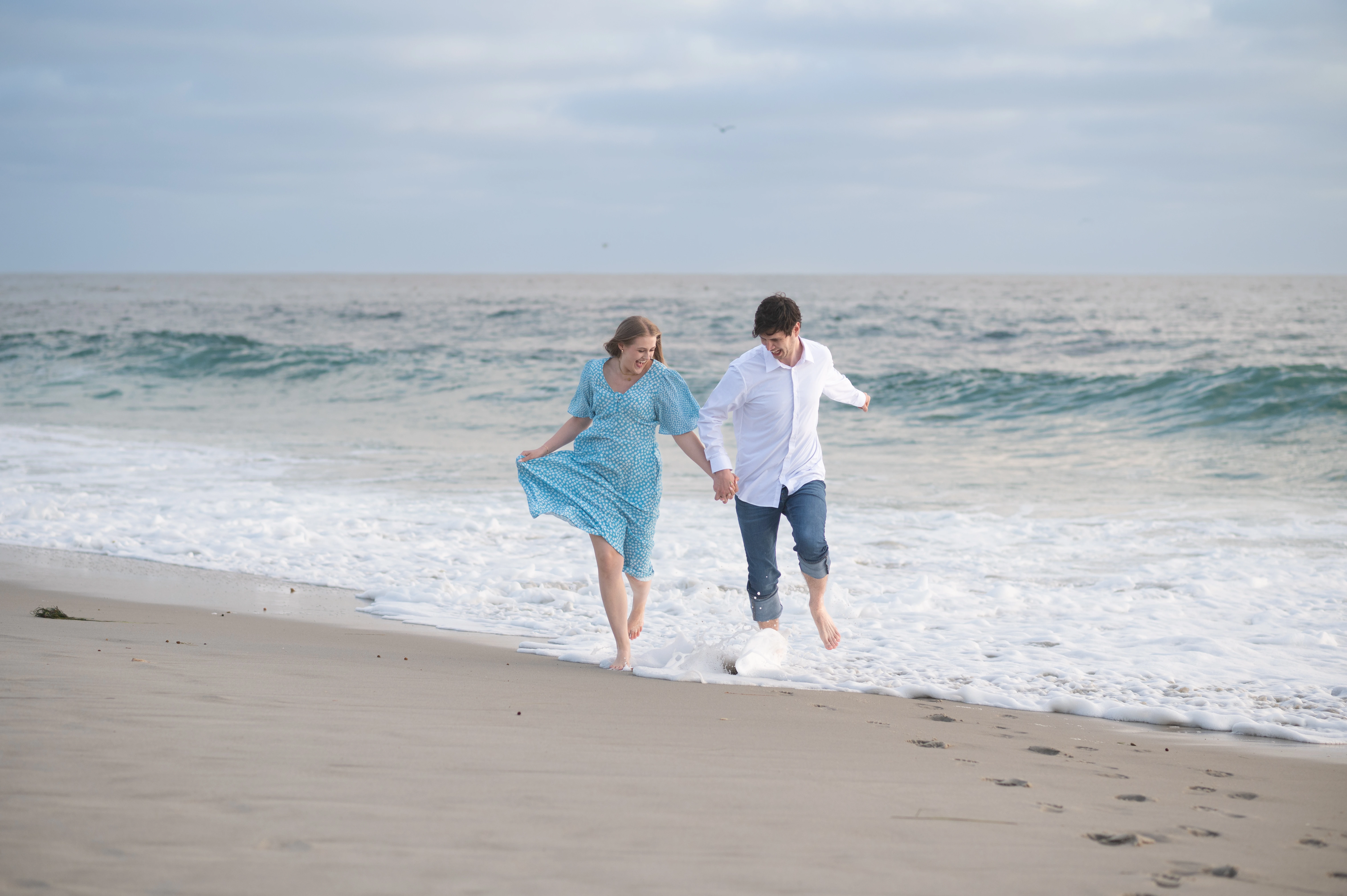 The couple joyfully runs along the shoreline, splashing in the waves while holding hands