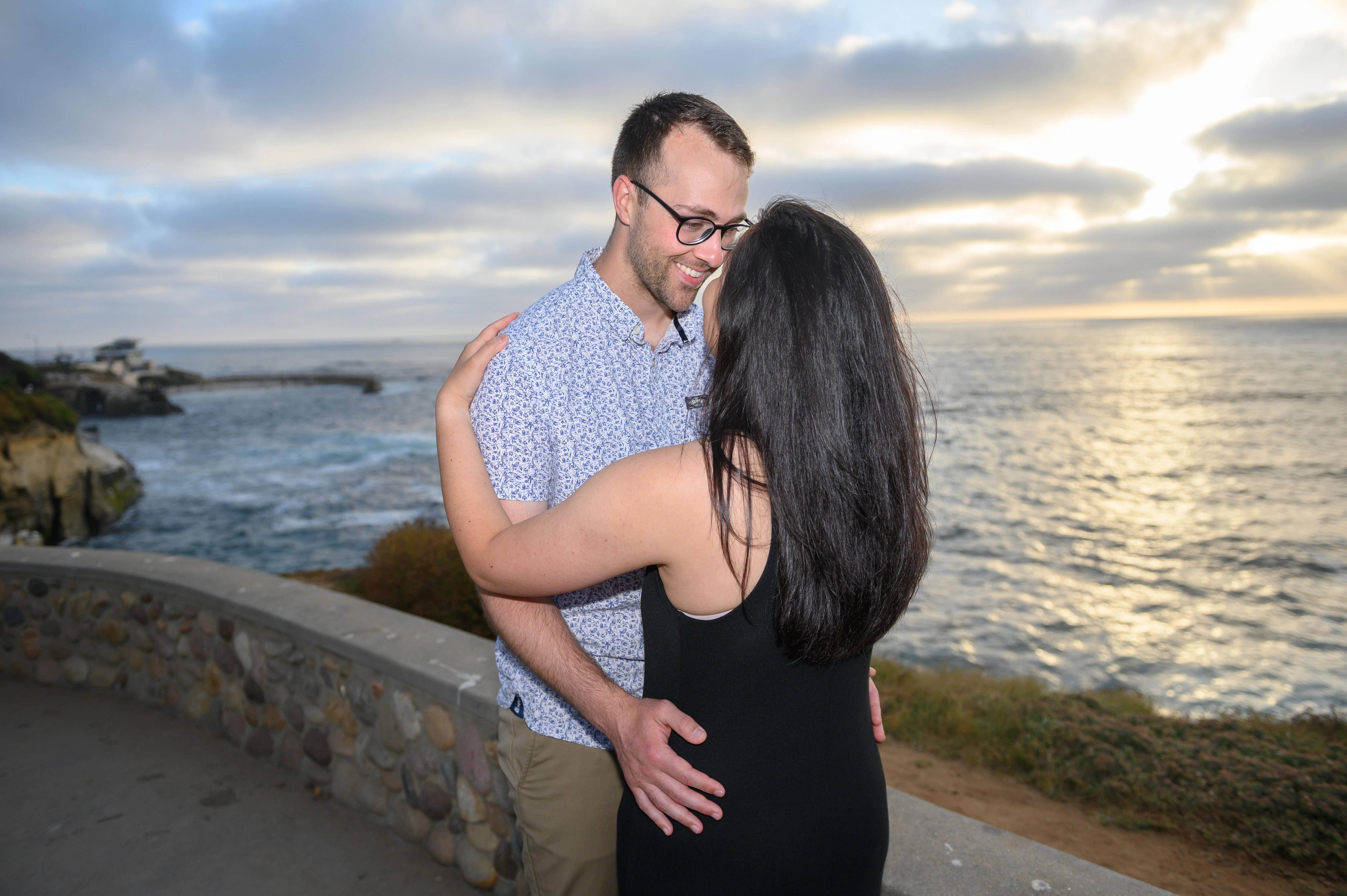 A couple embraces against a backdrop of a sunset reflecting on the water, sharing a tender moment