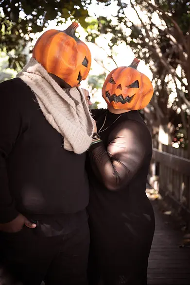 a couple with pumpkin heads sharing a playful moment in a San Diego Halloween photoshoot.