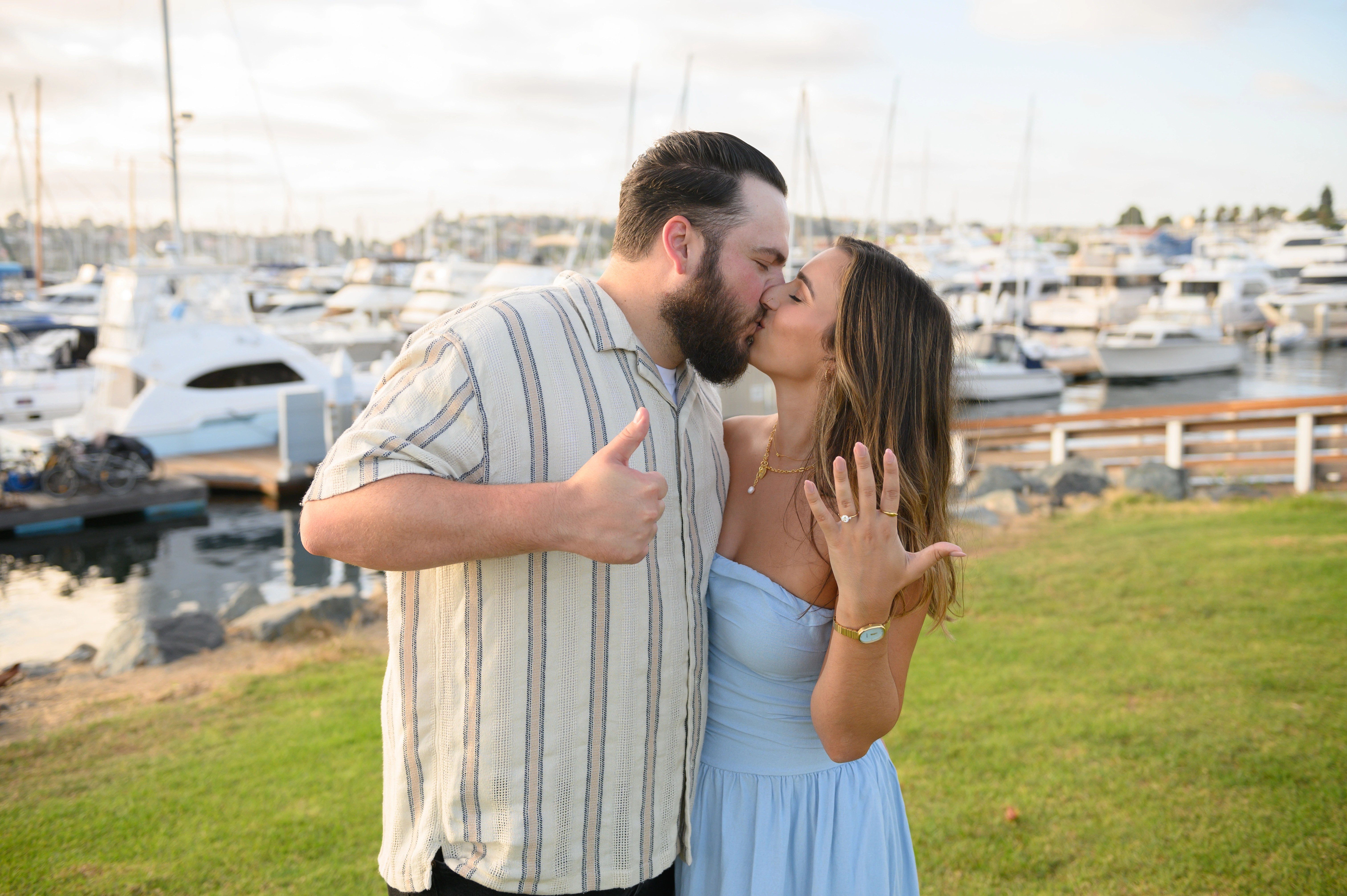 San Diego proposal photographer captures a romantic moment between a couple celebrating their engagement by the marina, showcasing the joy of love and commitment.