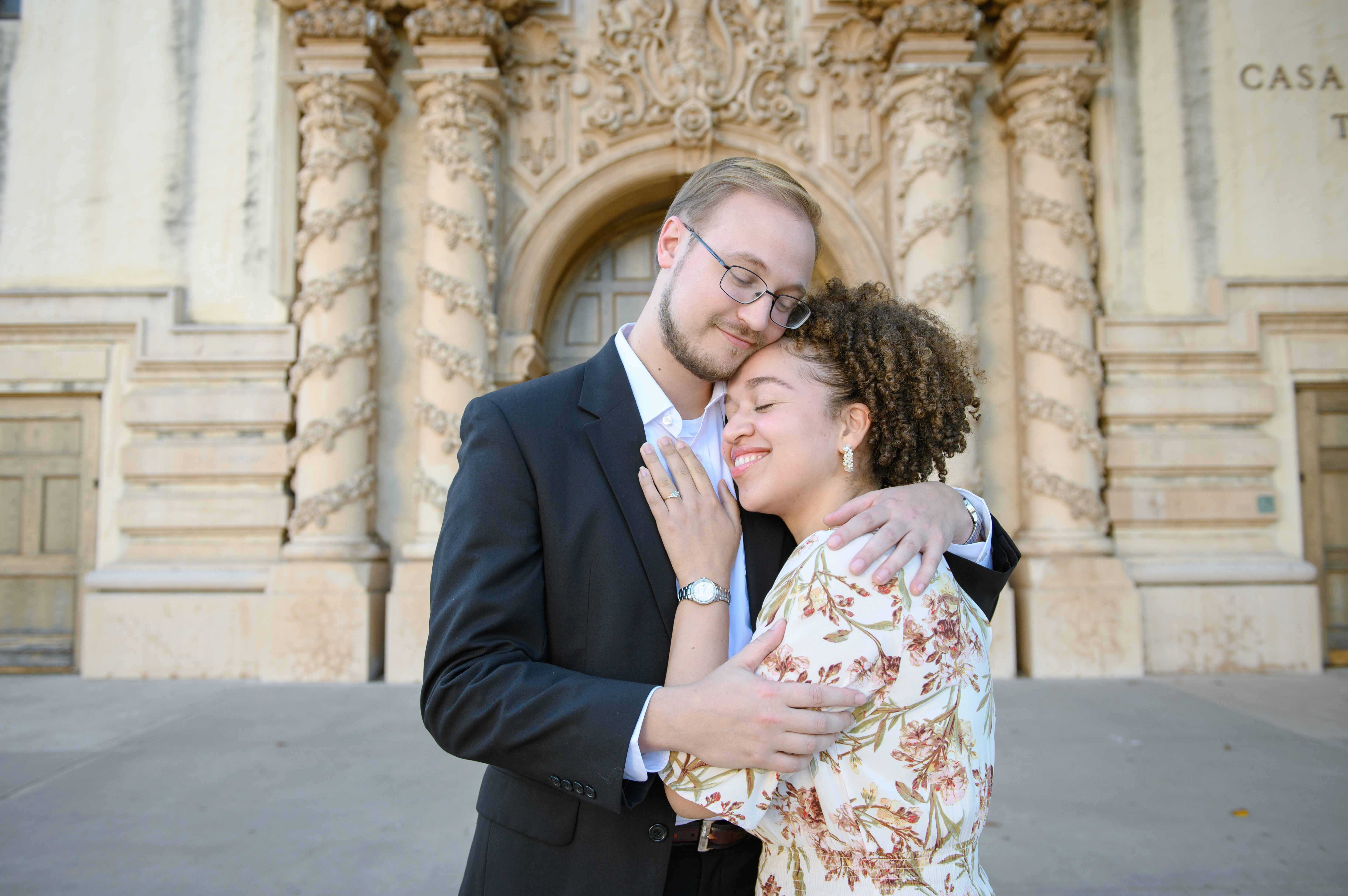A couple embraces in front of a beautifully ornate building, showcasing their affection in a romantic setting