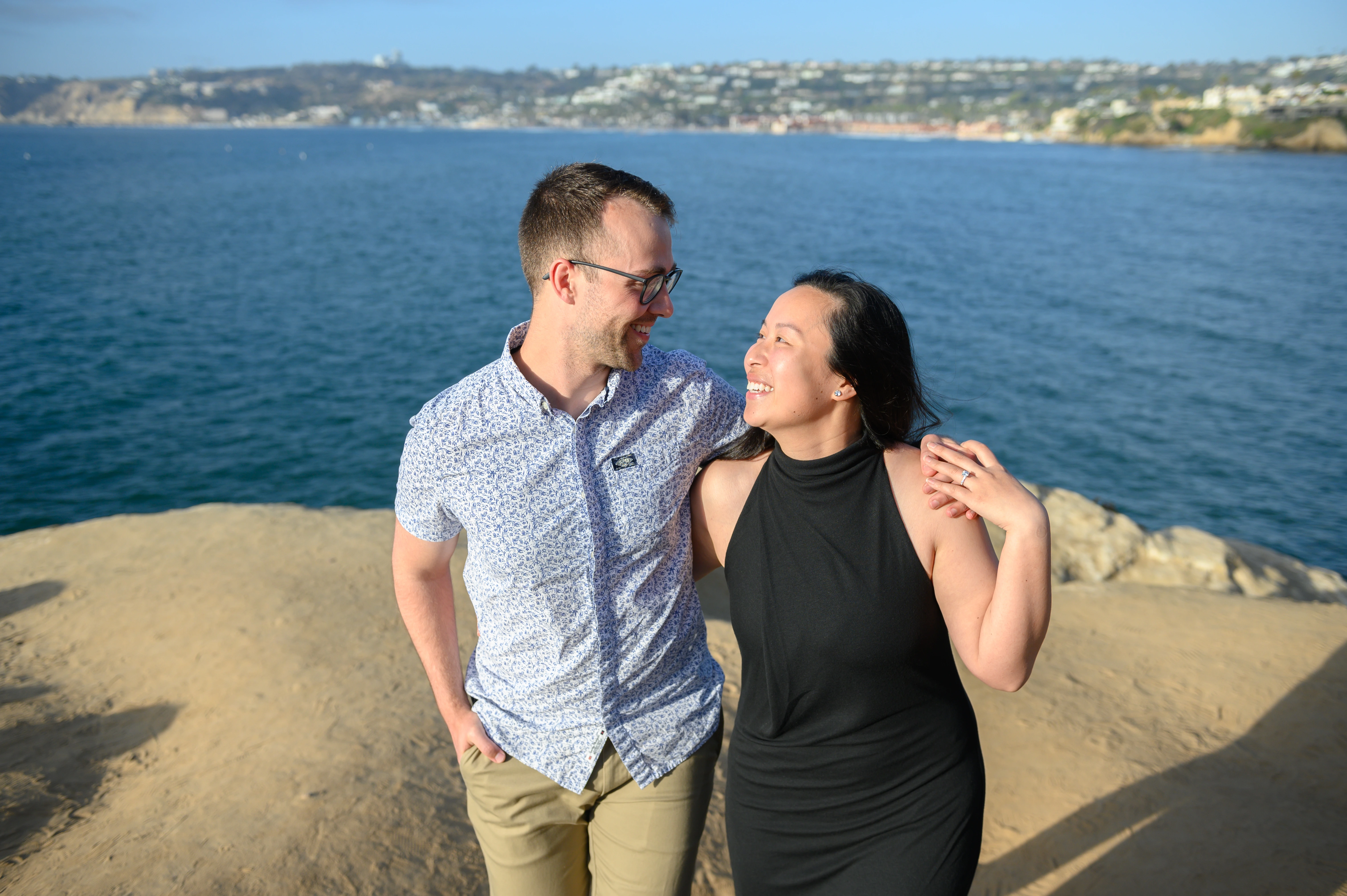 The couple poses together on a rocky outcrop with a scenic ocean view in the background