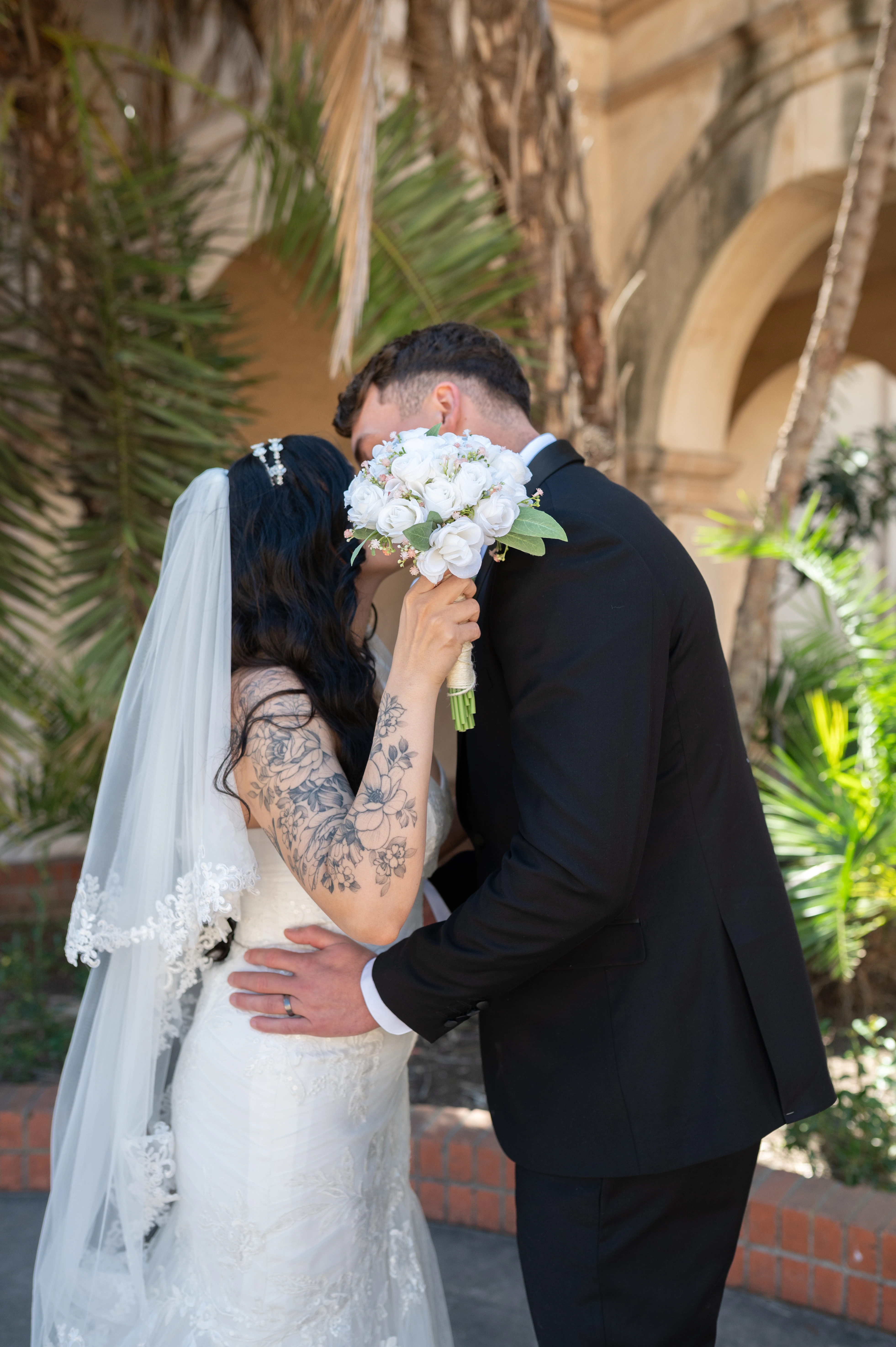 Couple sharing a kiss behind a bouquet of white flowers during their Balboa Park elopement in San Diego.