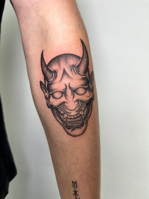 A Japanese Oni mask in shades of black and grey on a forearm by Molly at Paradise Tattoo High Wycombe 