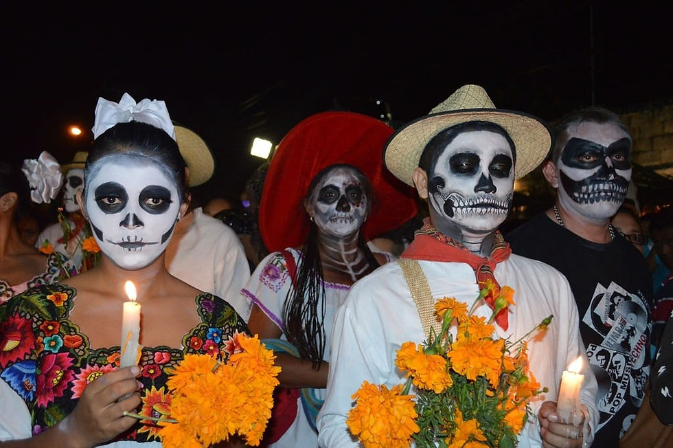 Procession of people with calavera make up and holding candles and flowers.