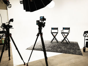 Empty film studio with cameras, softbox lights, gray rug, and two Myers Media director chairs on a white backdrop.