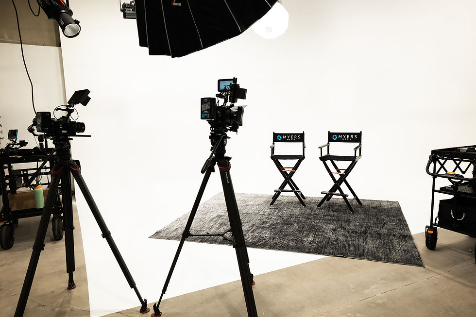 Empty film studio with cameras, softbox lights, gray rug, and two Myers Media director chairs on a white backdrop.