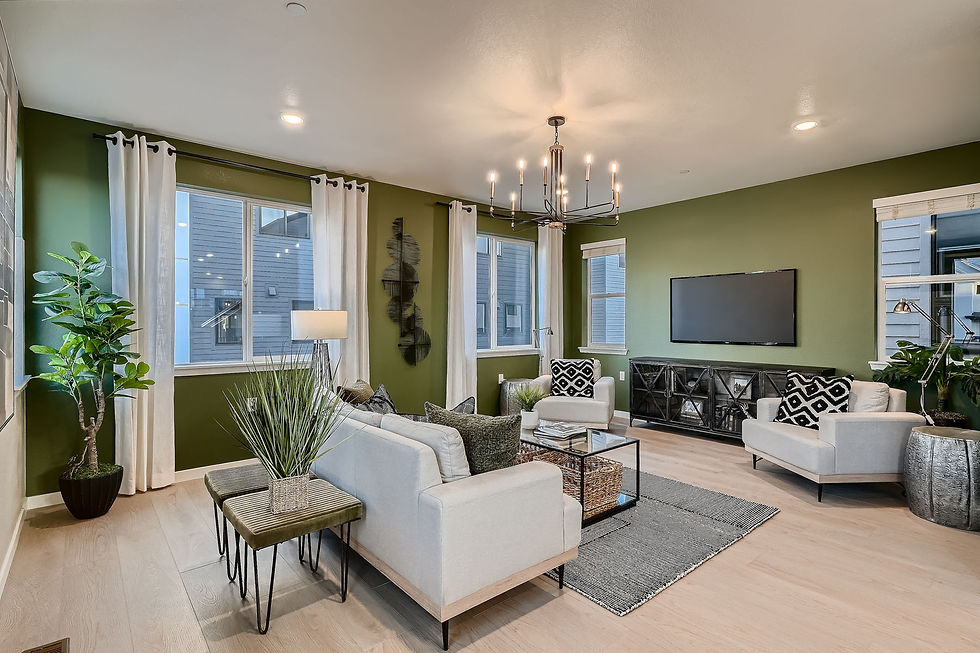 Open second-floor living area of the Soar plan with sectional sofa, green accent wall, TV, pendant light over dining table, large windows with drapes.