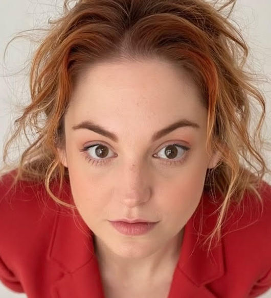 a red headed woman wearing red stares directly into the camera at an upward angle