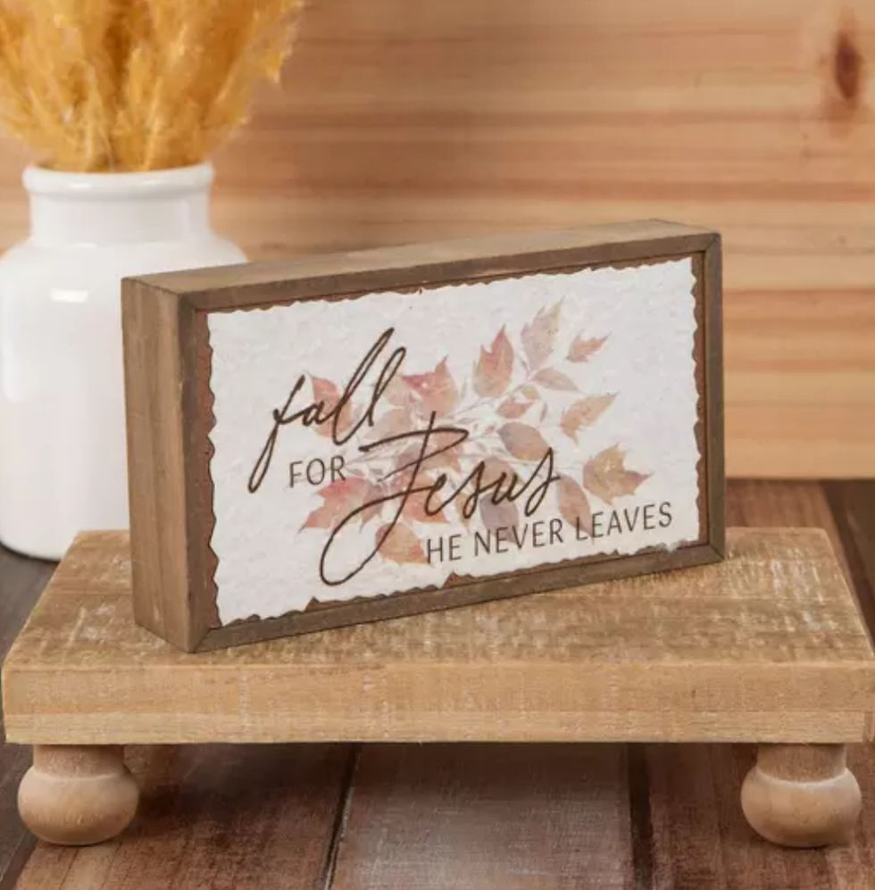Wooden plaque on stand reads, "fall for Jesus, He never leaves," with autumn leaves design. White vase in background, rustic wood setting.