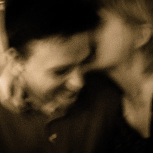 A pixelated, black-and-white photo of me and my wife laughing and kissing. We are at a bar in NYC.