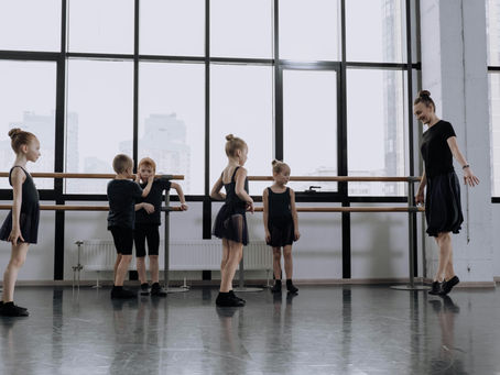 Dance teacher guiding young students at the barre, reflecting structured training and value-driven studio programs.