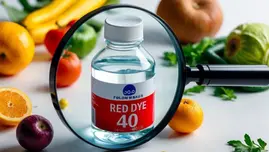 Red Dye 40 bottle examined under a magnifying glass with fresh fruits and vegetables in the background