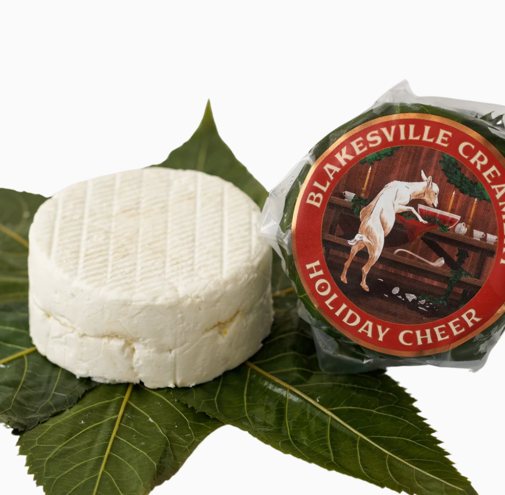 Unwrapped Holiday Cheer chevre on leave. Next to it a wheel of wrapped Holiday Cheer.