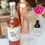 Thumbnail: Girl Meets Dirt Rhubarb shrub bottle next to a coupe glass with rhubarb shrub and a pink flower on the glass rim.