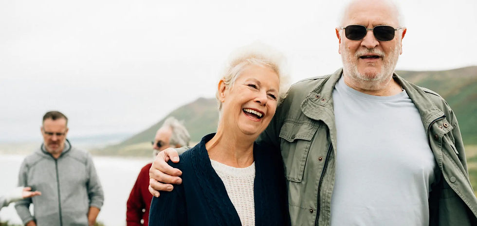 “Smiling older couple standing outdoors with friends, enjoying time together on a scenic hillside.”