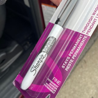 Close-up of a Sharpie Rub-a-Dub fine point laundry marker in its purple and white packaging, used for labeling bed sheet sizes.