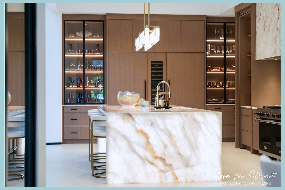 Luxury custom kitchen built by Jimmy Nash Homes featuring a marble waterfall island, brass pendant lighting, backlit glass cabinets, and custom appliance garage organized by Tara M. Stewart Professional Organizing.