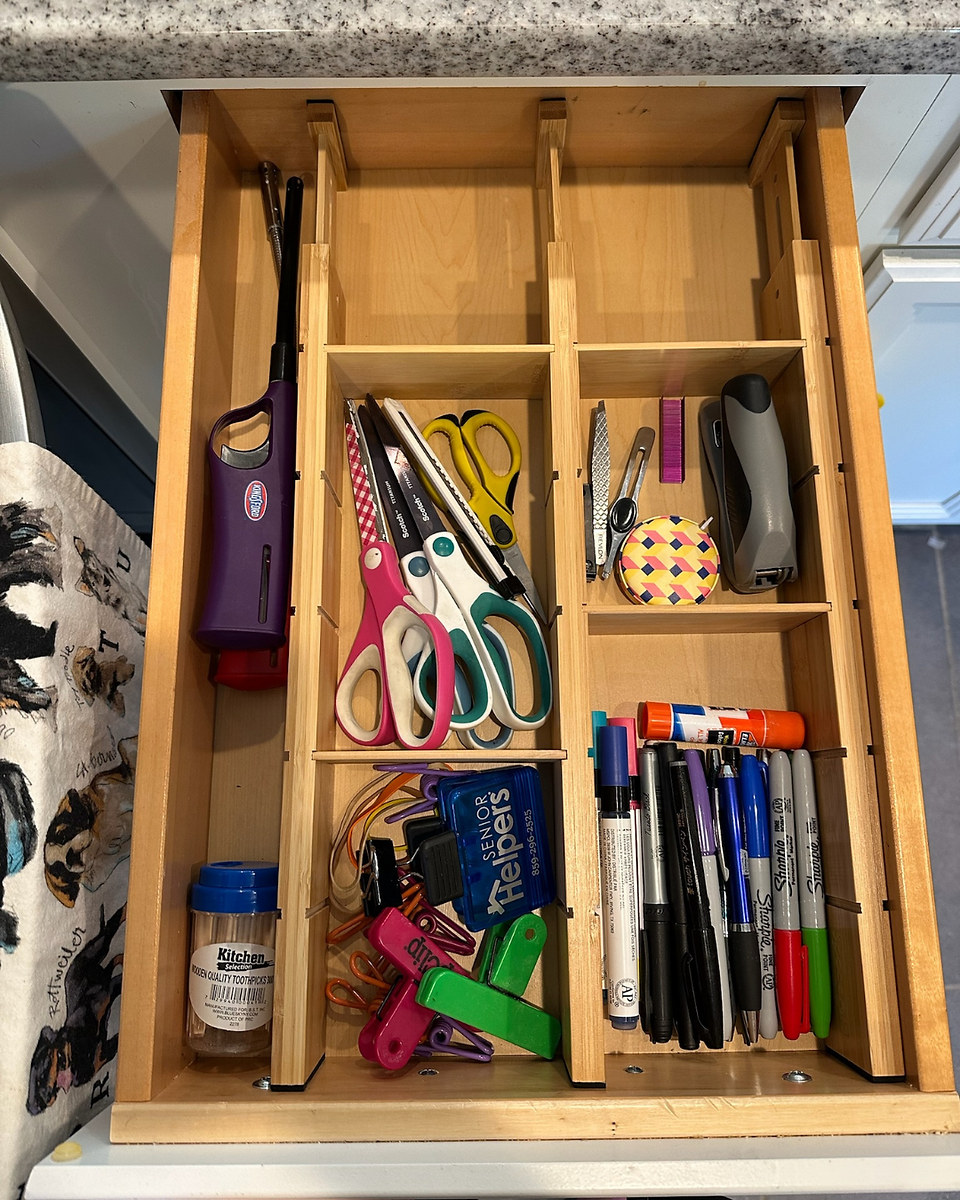 Open drawer with neatly organized junk drawer. Wooden dividers.