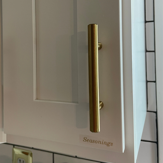 White kitchen cabinet doors in an Airbnb featuring gold handles and elegant gold lettering labels for seasonings