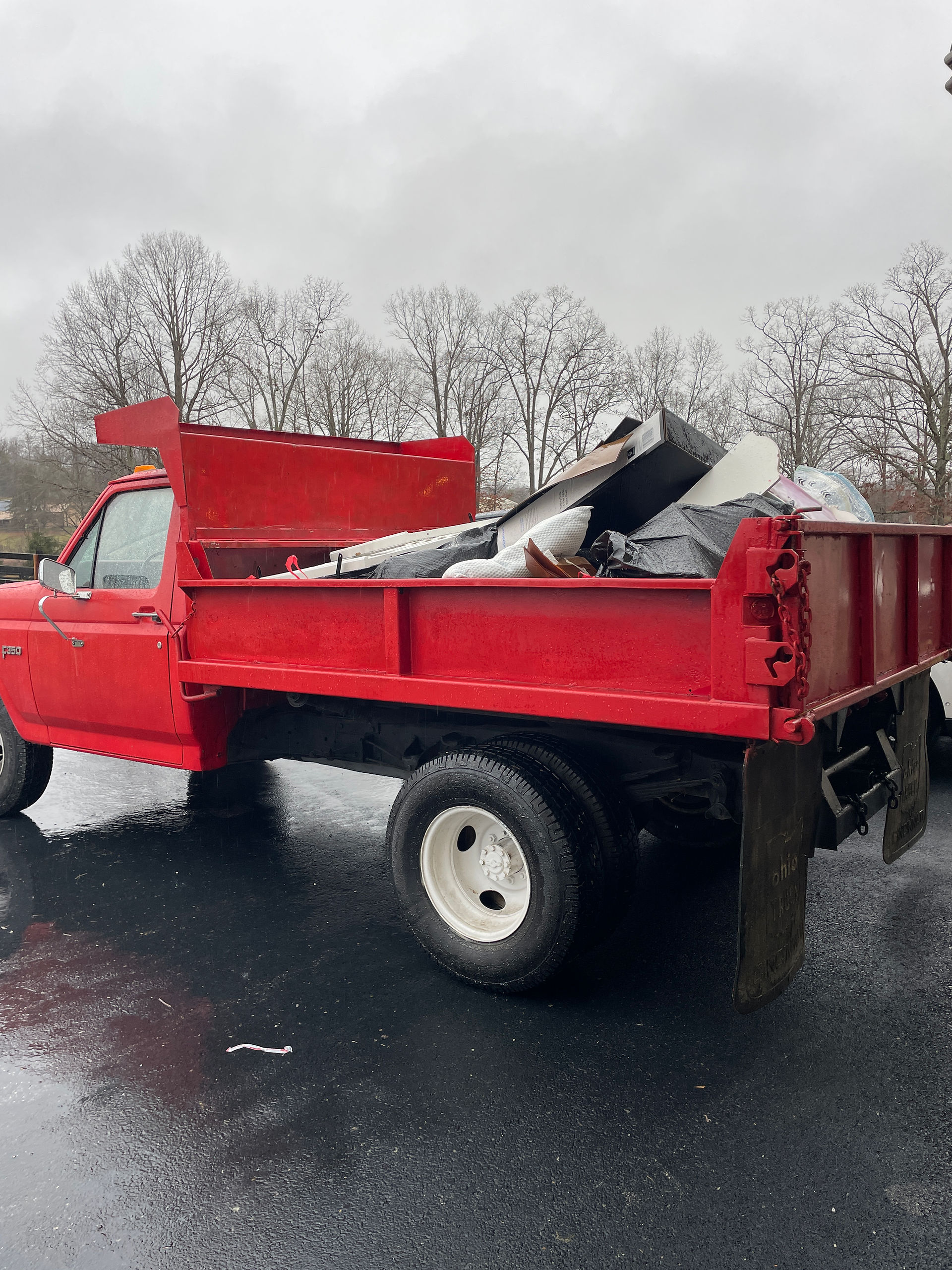 Red dump truck loaded with junk and furniture pieces during a rainy day garage clean-out