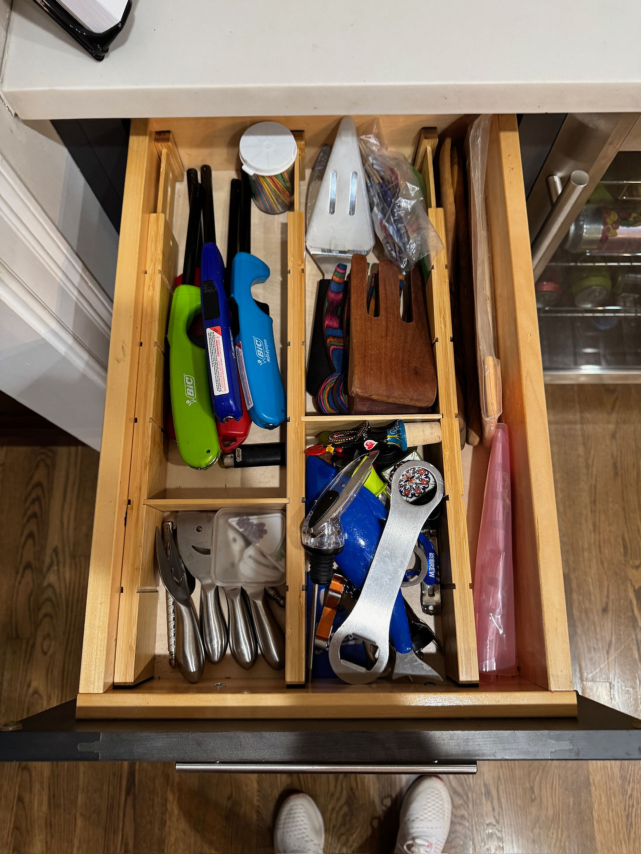 Open drawer with neatly organized compartments containing kitchen utensils and lighters. Wooden dividers.