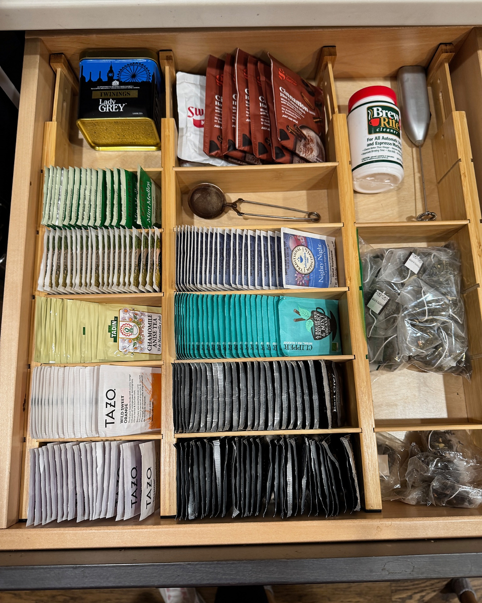 Open drawer with neatly organized compartments containing teas and drink mixes. Wooden dividers and labels for items.