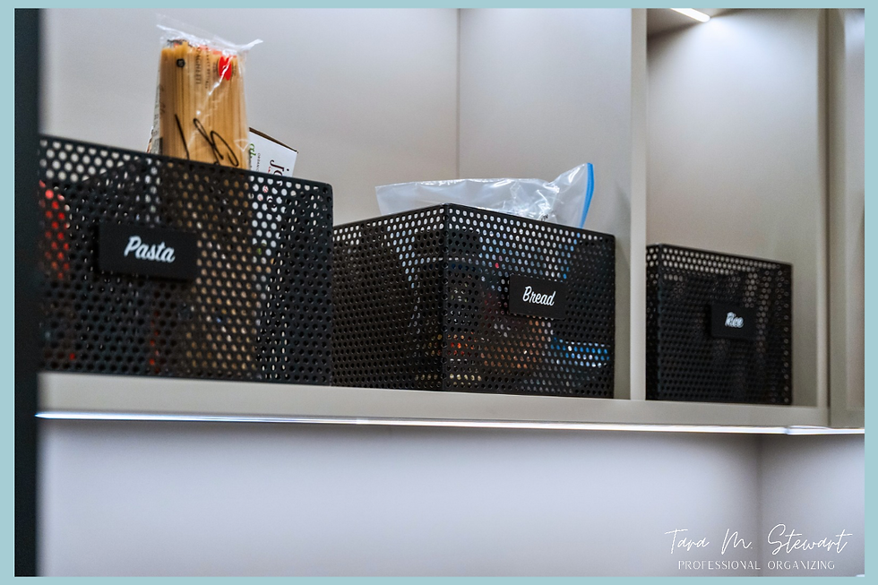 Black metal mesh pantry storage baskets with custom magnetic script labels for pasta, bread, and rice on backlit floating shelves, organized by Tara M. Stewart Professional Organizing