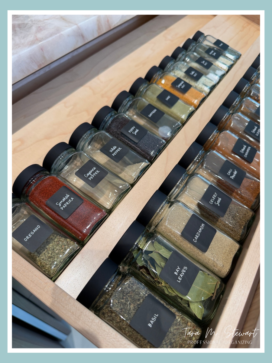 Custom organized kitchen spice drawer featuring uniform glass jars with custom black script labels set into built-in wooden inserts by Tara M. Stewart Professional Organizing.
