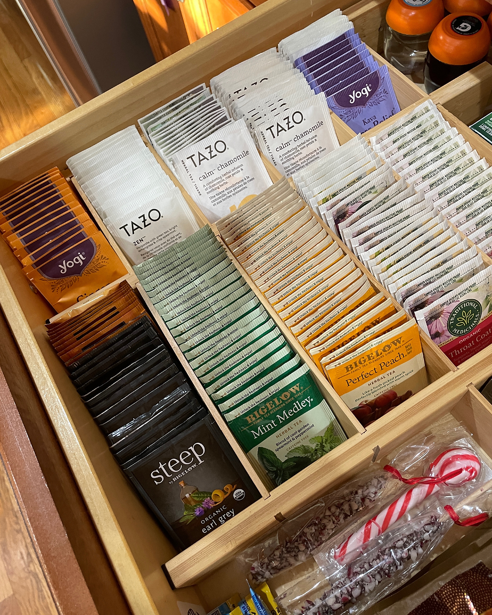 Open drawer with neatly organized compartments containing teas and drink mixes. Wooden dividers.