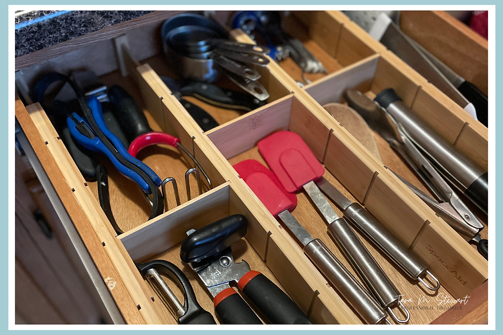 Kitchen drawer with organized utensils: red spatulas, measuring cups, peelers, and can openers. Wooden dividers, neat arrangement.