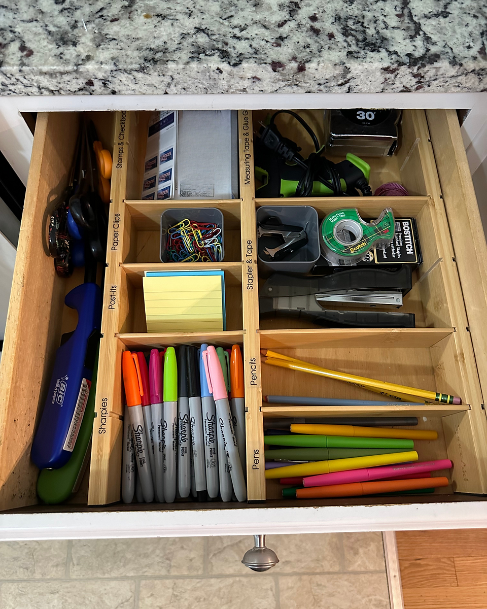 Open drawer with neatly organized junk drawer. Wooden dividers. Sharpies, post-it notes, stamps