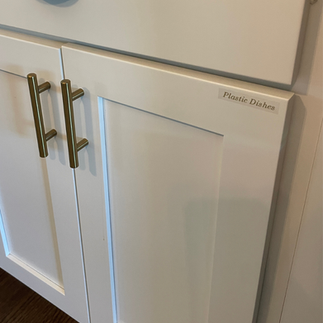 White kitchen cabinet doors in an Airbnb featuring gold handles and elegant gold lettering labels for dishes