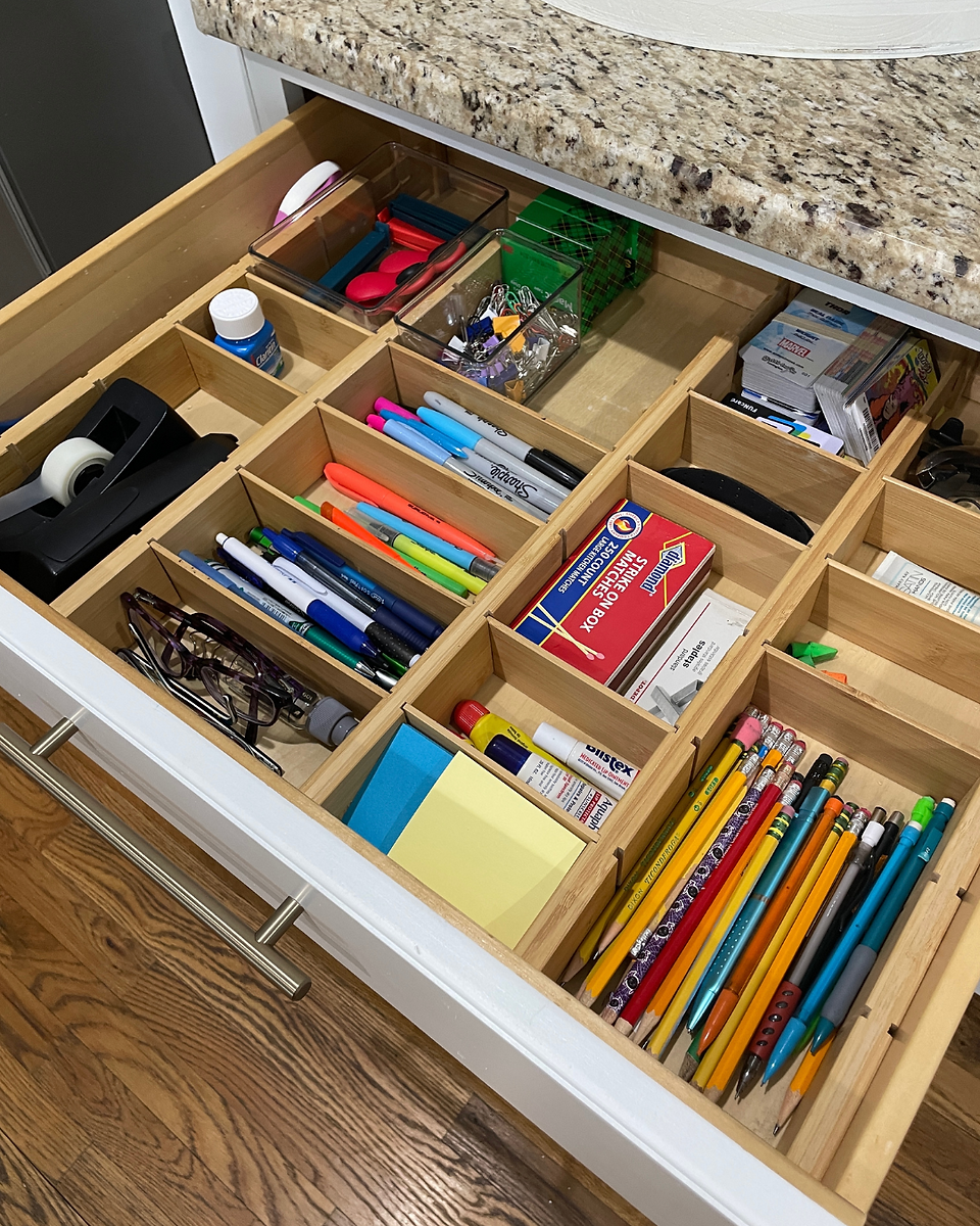 Open drawer with neatly organized junk drawer. Wooden dividers. Drawer containing pens, tape, glasses, pencils, chapstick