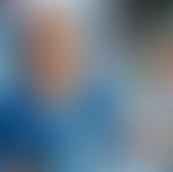 Smiling nurse in blue scrubs holds a syringe. Hospital bed, medical equipment, and heart monitor in the background. Calm setting.