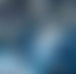 Two surgeons in blue scrubs and masks operate in a hospital room. Medical equipment displays data in the background. Focused mood.