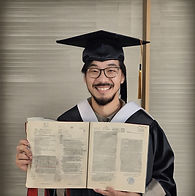 male Asian student in graduation cap and gown holding an academic project in his hands