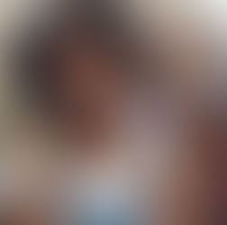 Smiling woman in denim overalls with friends in background. Outdoors, cozy atmosphere, beige building, casual attire, cheerful mood.