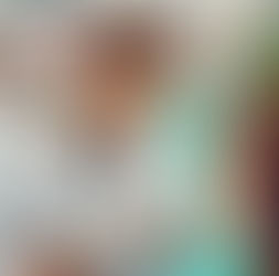 Dentist in white coat showing a dental model to a patient. Smiling staff in the background. Bright clinic with tooth posters.