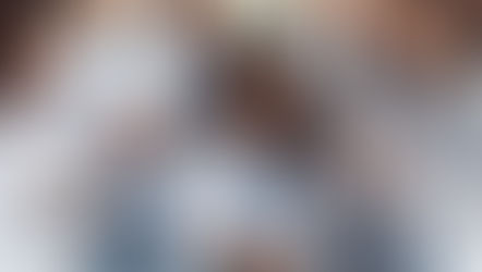 Nurses in white coats gather around a patient in a hospital bed, taking notes. The setting is calm with natural light streaming in.