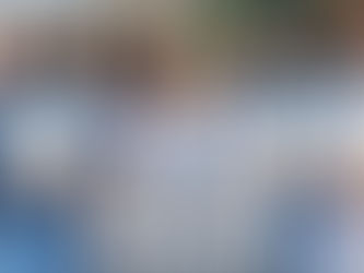 Group of diverse medical graduates in blue scrubs and white lab coats, smiling and holding diplomas. One holds a sign with jumbled text.