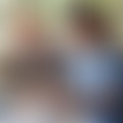 Elderly man and nurse smiling while working on a crossword puzzle at a table. Bright room with window, nurse in blue scrubs and stethoscope.