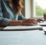 a woman at a table working on her laptop with a window in the background