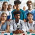 Students in lab coats and scrubs focus on a microscope in a science lab. Test tubes with colorful liquids surround them. Mood is attentive.
