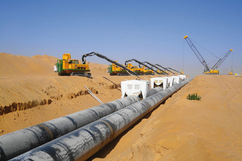 Yellow machinery installing large pipelines in a sandy desert under a clear blue sky. Cranes and sand dunes visible in the background.