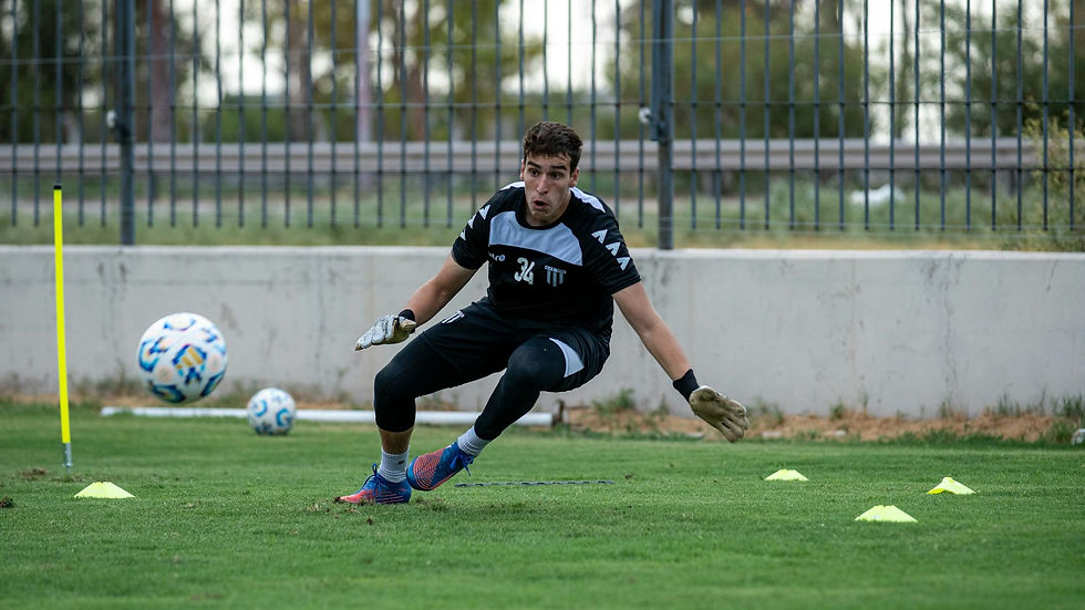 A young male goalkeeper practicing on a grass field outdoors, focusing on agility and training skills.