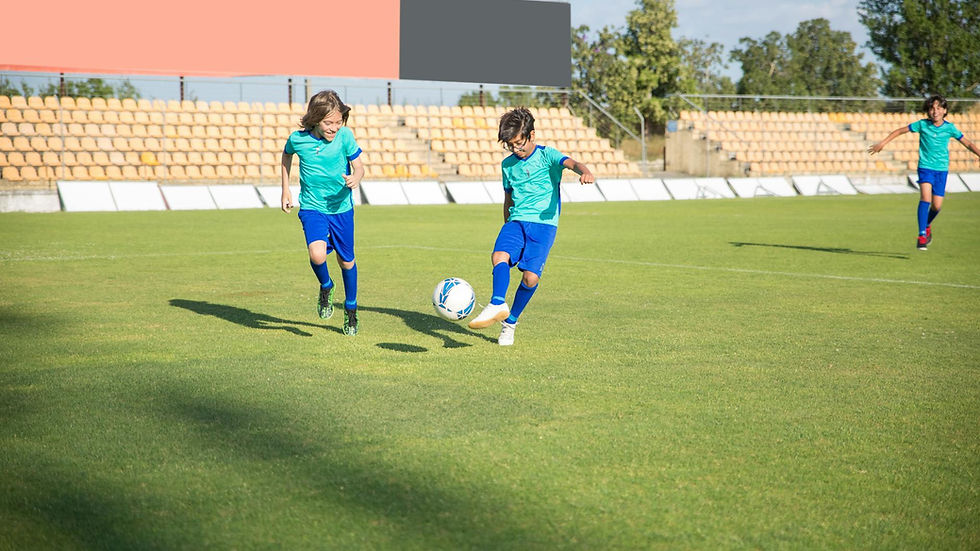 Children playing football on a sunny day in a Portuguese stadium.