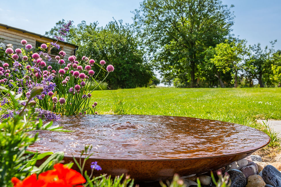A low corten steel bowl with water bubbling and cascading over the sides onto pebbles adds a real feature to the garden 